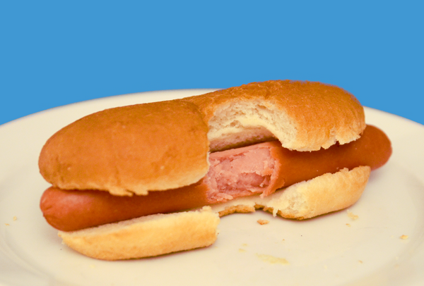 Disgusting, unseasoned hot dog with a bite taken from the middle. White, crummy plate, blue background