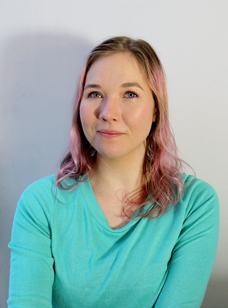 Lightly smiling, pink-haired editor-in-chief photographed on a boring white background