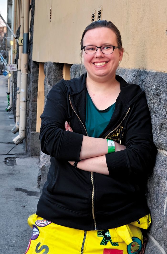 Mari Karlsson kuvattuna Helsingin kadulla haalareissa ja TKO-äly-hupparissa hymyileväisenä